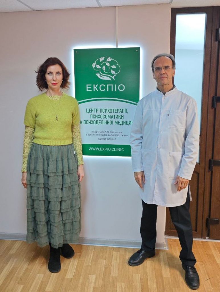 Intertwined Founder and CEO Svitlana Iniakoviene and Dr Vladislav Matrenitsky are standing next to a backlit Expio sign, inside the clinic.